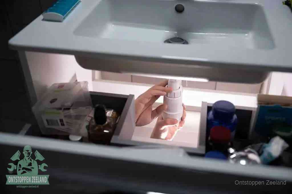 Een pompfles met zeep boven een wastafel, de heet water en afwasmiddel-methode om een vetprop in de afvoer los te maken in Zeeland