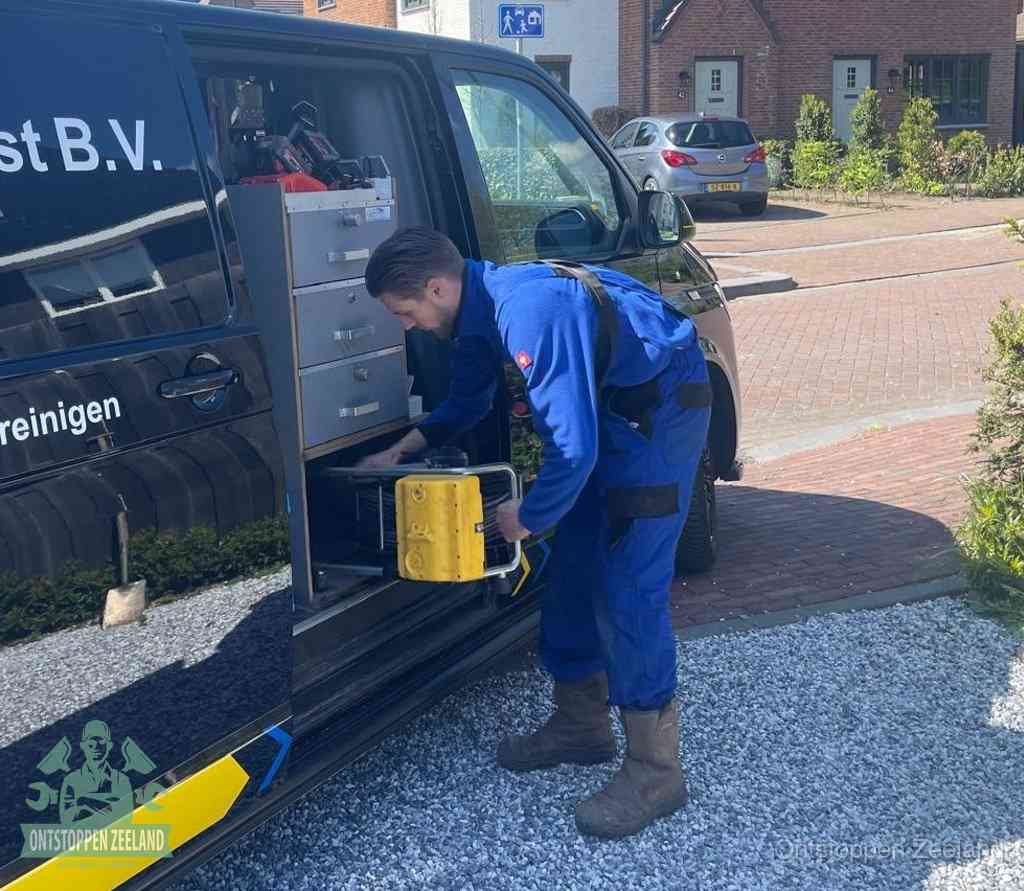 Een monteur pakt buiten op de oprit gereedschap uit de bedrijfsbus, het moment om een professional in te schakelen voor een verstopte afvoer in Zeeland