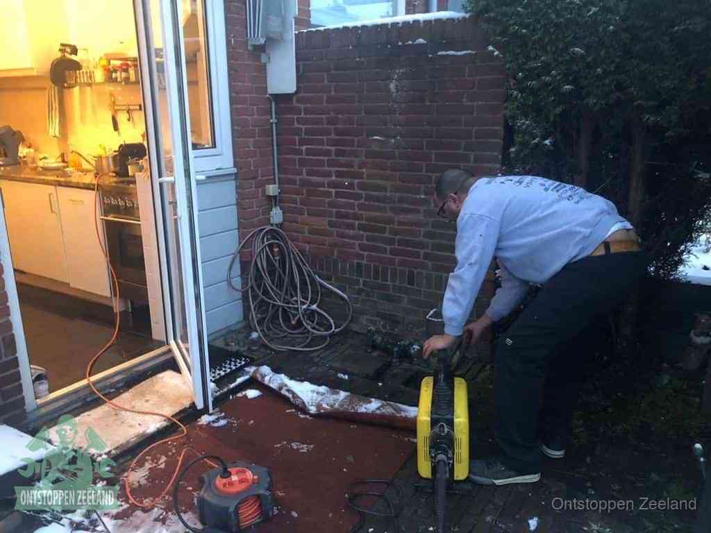 Een monteur werkt buiten bij een open riool-/grondput met een elektrische ontstoppingsmachine om een verborgen afvoerprobleem op te sporen in Zeeland