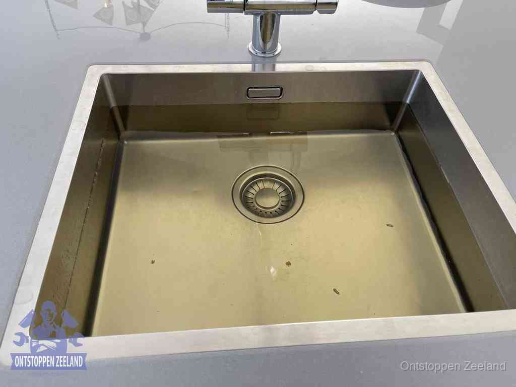 Stilstaand water in een rvs spoelbak dat niet wegloopt, een duidelijk signaal van een gootsteenverstopping in Zeeland