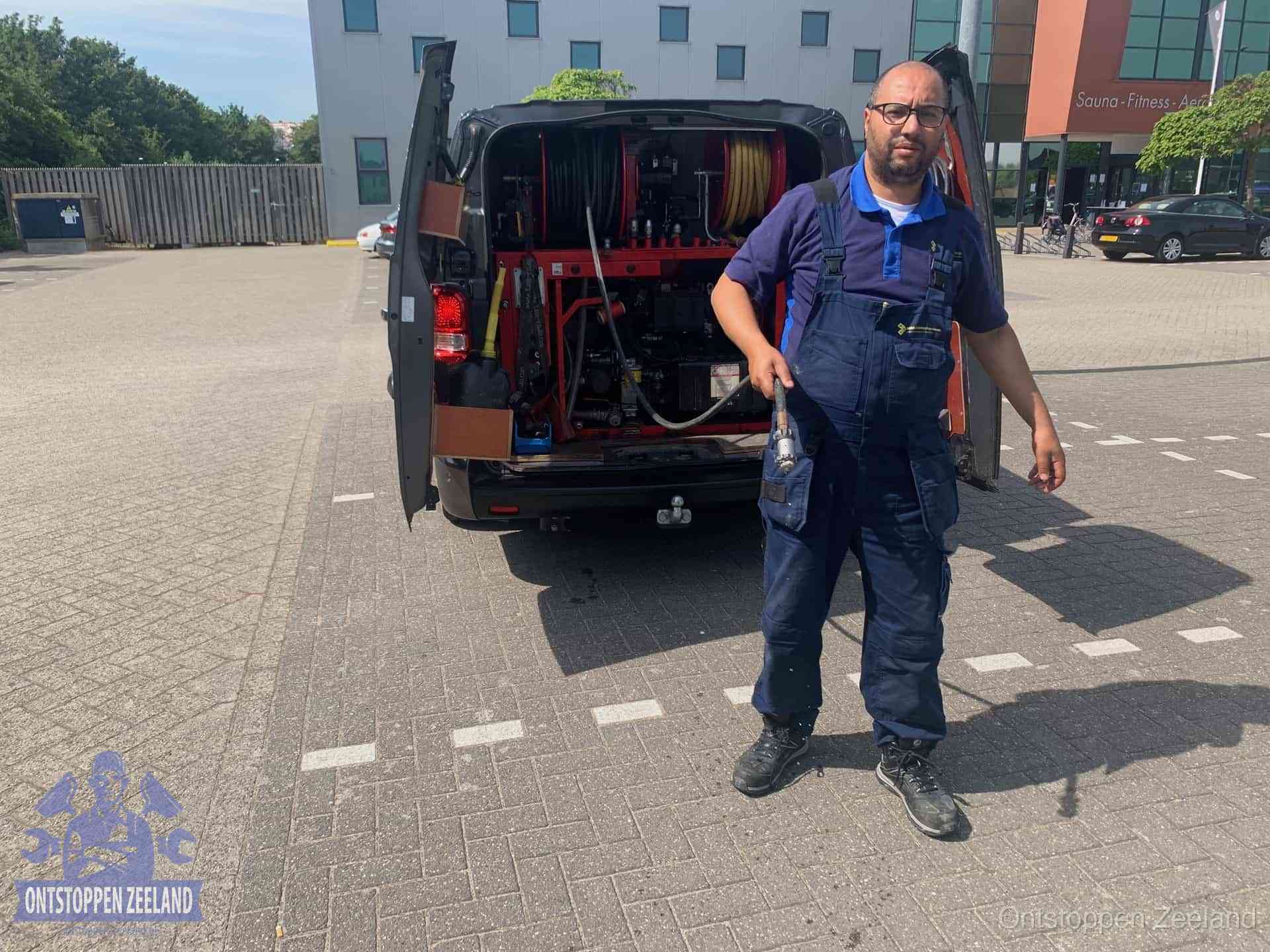 Een monteur bij zijn bestelbus met een hogedruk- en rioolreinigingsunit, klaar om de oorzaak van terugkerende wc-verstoppingen aan te pakken in Zeeland