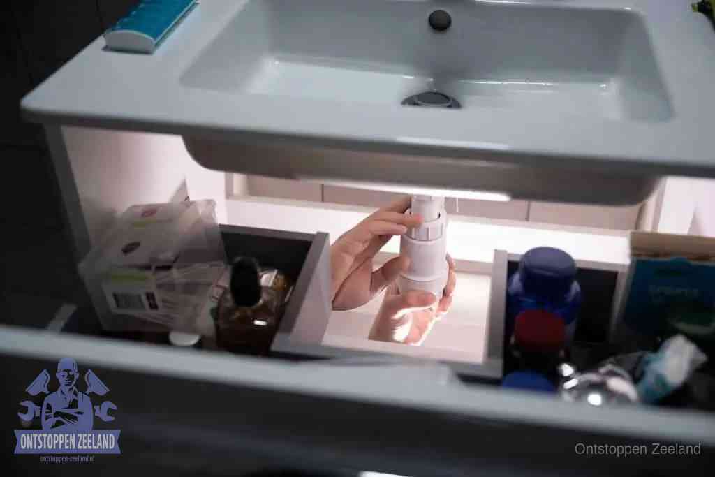 Een pompfles met zeep boven een wastafel in de toiletruimte, de warm water en afwasmiddel-methode om de wc te ontstoppen in Zeeland