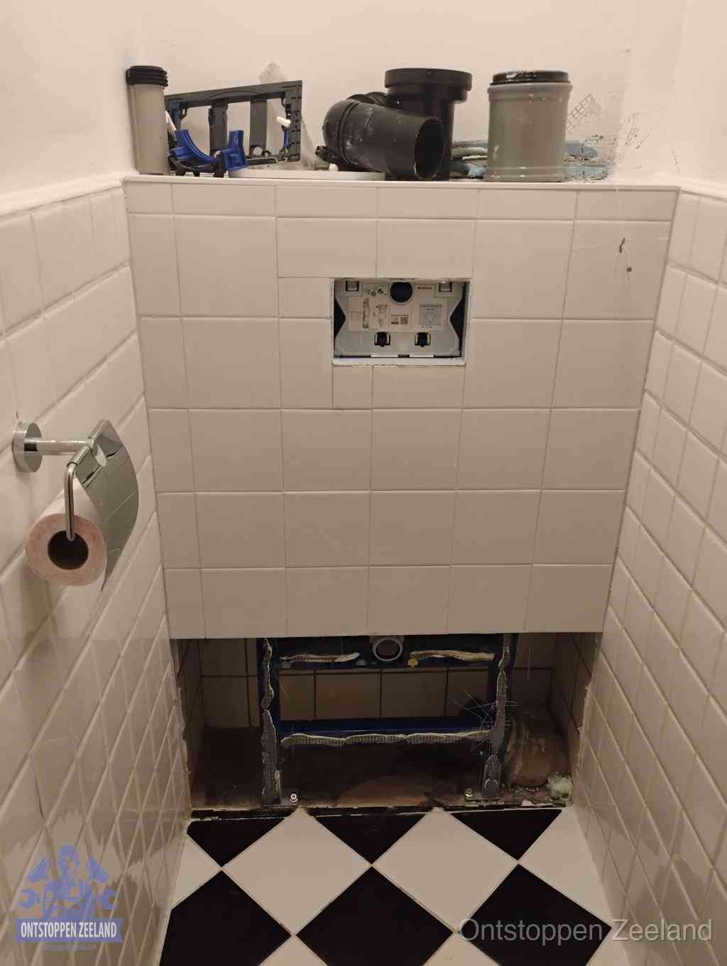 Een toiletruimte waar het hangtoilet en de inbouwreservoir-onderdelen zijn vrijgelegd voor onderhoud, periodiek nazicht voorkomt een wc-verstopping in Zeeland