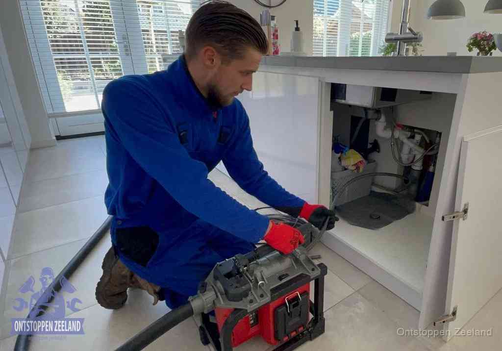 Een monteur voert een professionele elektrische ontstoppingsmachine in de afvoer onder de spoelbak tijdens het gootsteen ontstoppen in Zeeland